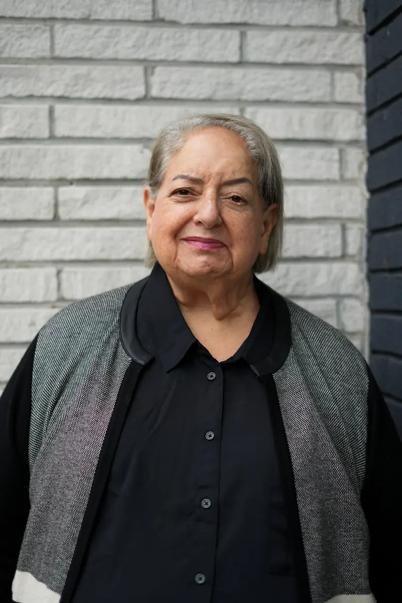 Sharon Tabak smiling, standing in front of a white brick wall